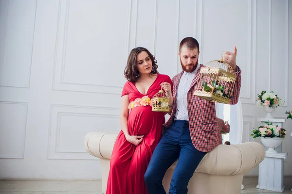 Krásný mladý pár v lásce. Těhotná žena se svým manželem sedí doma. Jsou s úsměvem a při pohledu na fotoaparát. Muž drží klíče k bytu a dívka holubník. — Stock fotografie