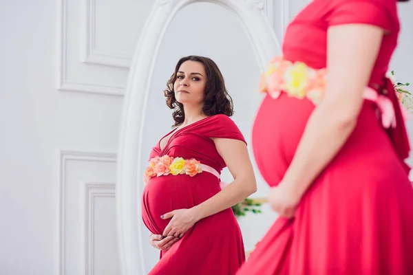 Bella donna incinta guardando nello specchio nella stanza della luce — Foto Stock