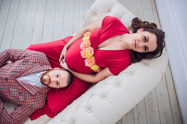 Молода красива вагітна пара сидить на старовинному дивані вдома — стокове фото