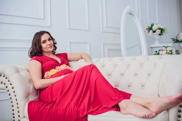 Donna incinta con un vestito rosso sdraiata sul divano — Foto Stock