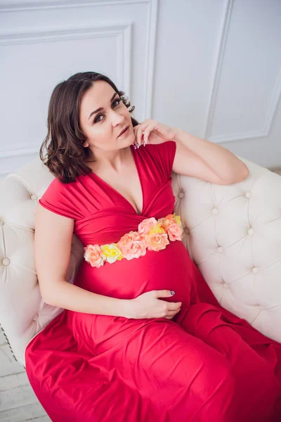 ソファーで横になっている赤いドレスに妊娠中の女性 — ストック写真