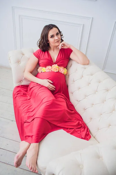 Donna incinta con un vestito rosso sdraiata sul divano — Foto Stock