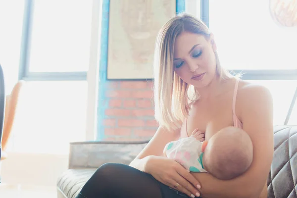 Amamantar Mujer lactante bebé en el interior del loft moderno. Diseño escandinavo minimalista. joven madre en ropa deportiva, entrenamiento en casa . —  Fotos de Stock