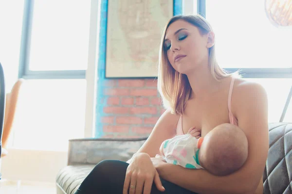 Mujer amamantando bebé en el interior del loft moderno. Diseño escandinavo minimalista. joven madre en ropa deportiva, entrenamiento en casa . — Foto de Stock