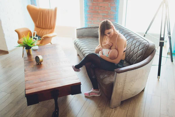 Szoptató nő szoptatás baba modern tetőtéri belső. Minimalista skandináv design. fiatal anya sportruházat, edzés otthon. — Stock Fotó