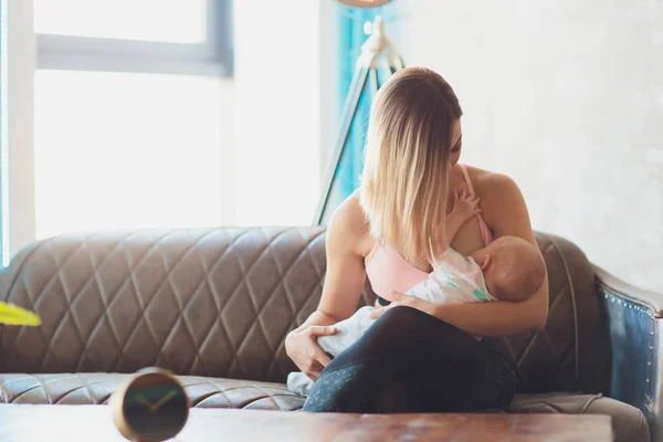 Amamantar Mujer lactante bebé en el interior del loft moderno. Diseño escandinavo minimalista. joven madre en ropa deportiva, entrenamiento en casa . —  Fotos de Stock