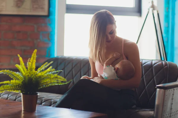 Mujer amamantando bebé en el interior del loft moderno. Diseño escandinavo minimalista. joven madre en ropa deportiva, entrenamiento en casa . —  Fotos de Stock