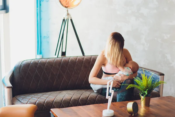 Mujer amamantando bebé en el interior del loft moderno. Diseño escandinavo minimalista. joven madre en ropa deportiva, entrenamiento en casa . —  Fotos de Stock