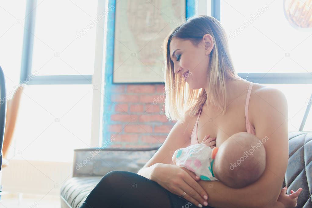 Woman breast feeding baby in modern loft interior. Minimalistic scandinavian design. young mother in sportswear, workout at home.