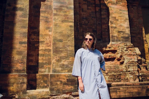 Mladá dívka v modrém šatu proti pozadí chrámu zdi v sluneční brýle. Moderní pojetí náboženství — Stock fotografie
