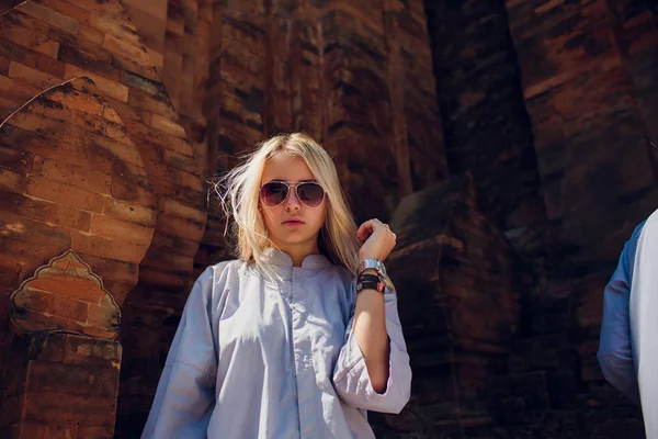 Молода дівчина в блакитному халаті на фоні стіни храму в сонцезахисних окулярах. Концепції МОДЕРН РІГІЯ — стокове фото