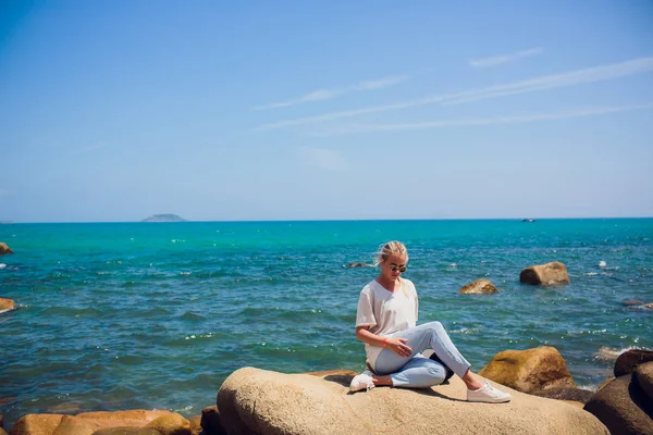 Mulher viajante senta-se e olha para a borda do penhasco na baía do mar — Fotografia de Stock