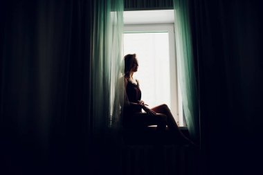 karanlık bir odada bir pencere yakınında bir düğün peçe kız