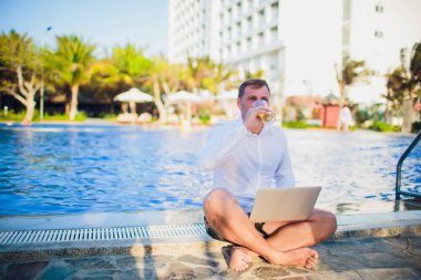 İşadamı takım elbise, bir elinde bir dizüstü bilgisayar ve bir bira, palet, açık mavi okyanus ile çevrili giyen okyanus şişme bir gemide başka bir kravat