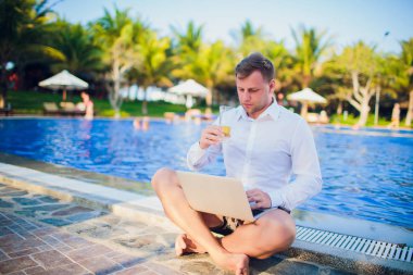 İşadamı takım elbise, bir elinde bir dizüstü bilgisayar ve bir bira, palet, açık mavi okyanus ile çevrili giyen okyanus şişme bir gemide başka bir kravat