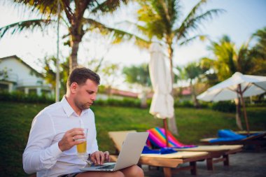 İşadamı takım elbise, bir elinde bir dizüstü bilgisayar ve bir bira, palet, açık mavi okyanus ile çevrili giyen okyanus şişme bir gemide başka bir kravat
