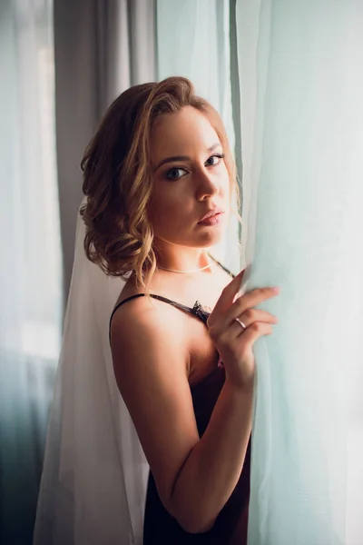 Chica en un velo de boda cerca de una ventana en una habitación oscura —  Fotos de Stock