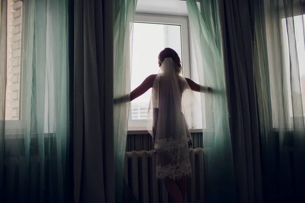Ragazza in un velo nuziale vicino a una finestra in una stanza buia — Foto Stock