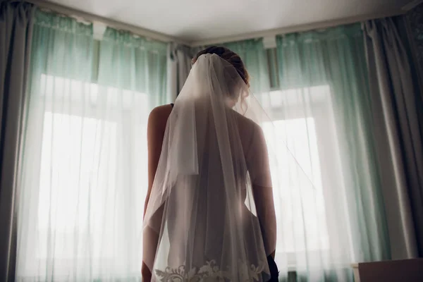 Flicka i ett bröllop slöja nära ett fönster i ett mörkt rum — Stockfoto