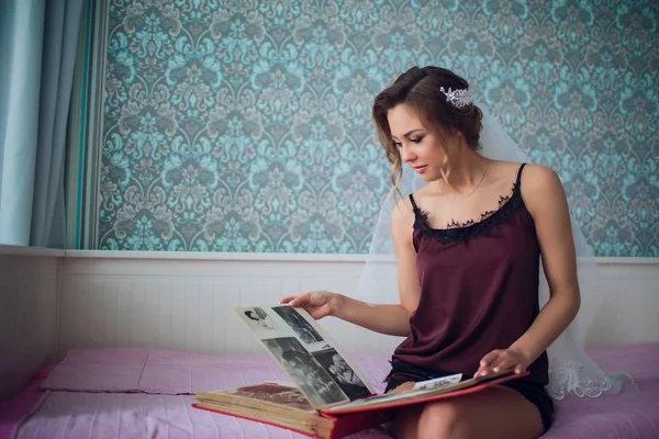 Chica en un velo de boda viendo sus hijos álbum de fotos en una habitación oscura — Foto de Stock