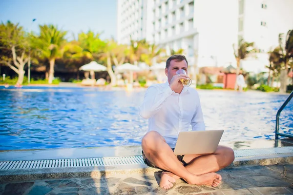 İşadamı takım elbise, bir elinde bir dizüstü bilgisayar ve bir bira, palet, açık mavi okyanus ile çevrili giyen okyanus şişme bir gemide başka bir kravat