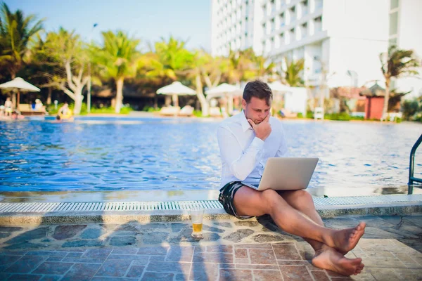 İşadamı takım elbise, bir elinde bir dizüstü bilgisayar ve bir bira, palet, açık mavi okyanus ile çevrili giyen okyanus şişme bir gemide başka bir kravat