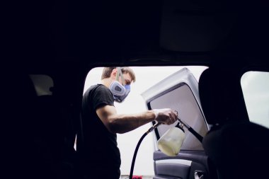 Yakışıklı adam sıcak buharla araba temizliyor.