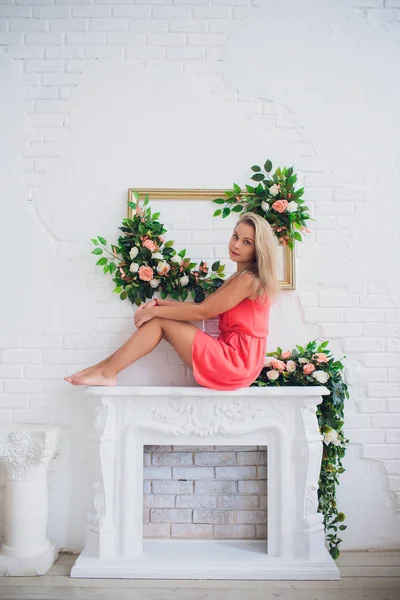 Joven mujer rubia atractiva cerca de la chimenea de Navidad en el interior acogedor hogar. Chica adolescente en vestido rojo. Concepto de vacaciones de invierno. Hermosa decoración blanca —  Fotos de Stock