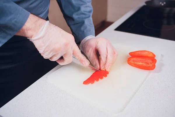 Rebanando pimiento rojo dulce en la tabla de cortar. la mano masculina corta el pimiento con cuchillo. Vista desde arriba — Foto de Stock