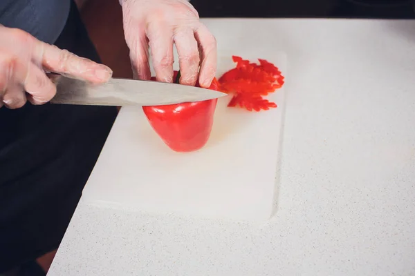 Rebanando pimiento rojo dulce en la tabla de cortar. la mano masculina corta el pimiento con cuchillo. Vista desde arriba — Foto de Stock