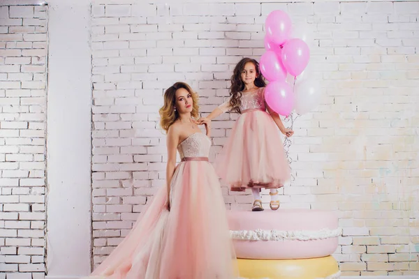 Anne ve kızı lüks, pembe, yeşil elbiseler. Aile kıyafetler, aynı elbiseler. Arka plan güzel, pahalı, beyaz, klasik iç kısmıdır. Sanat, aile fotoğraf.