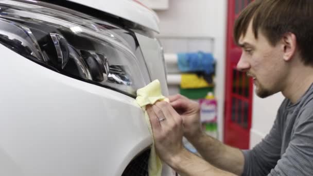 Primer plano de las manos del hombre que despegan la película con la capucha blanca coche caro. Esta película protege el vehículo de la pintura en bruto . — Vídeo de stock