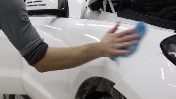 Gros plan des mains de l'homme qui décollent le film avec une voiture de luxe à capot blanc. Ce film protège le véhicule de la peinture rugueuse . — Video