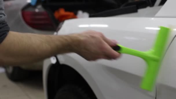 Gros plan des mains de l'homme qui décollent le film avec une voiture de luxe à capot blanc. Ce film protège le véhicule de la peinture rugueuse . — Video