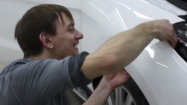 Close up shot of the hands of man who unstick the film with white cowl expensive car. This film protects the vehicle from the rough painting. — Stock Video