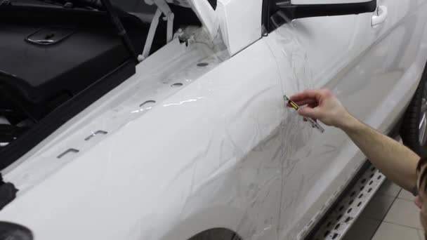 Gros plan des mains de l'homme qui décollent le film avec une voiture de luxe à capot blanc. Ce film protège le véhicule de la peinture rugueuse . — Video