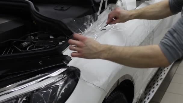 Close up shot of the hands of man who unstick the film with white cowl expensive car. This film protects the vehicle from the rough painting. — Stock Video