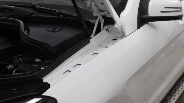 Gros plan des mains de l'homme qui décollent le film avec une voiture de luxe à capot blanc. Ce film protège le véhicule de la peinture rugueuse . — Video
