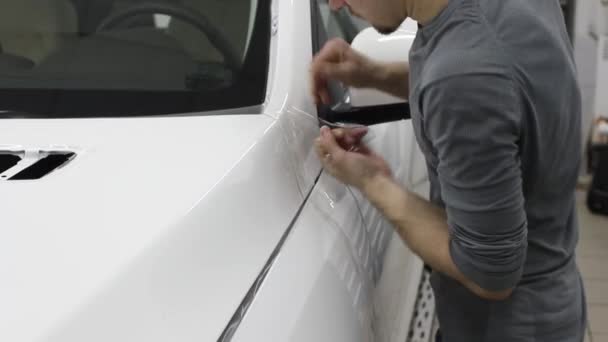 Gros plan des mains de l'homme qui décollent le film avec une voiture de luxe à capot blanc. Ce film protège le véhicule de la peinture rugueuse . — Video