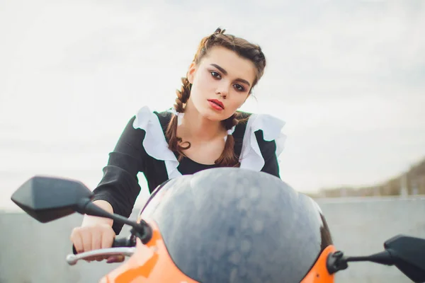 Colegiala de pie con delantal uniforme blanco marino típico se sienta en motocicleta —  Fotos de Stock
