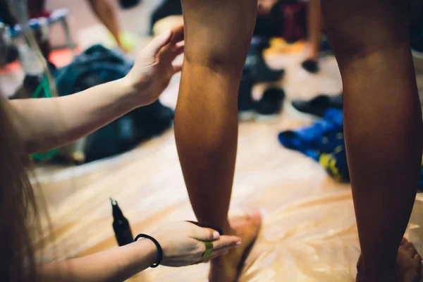 Bodybuilding competition backstage: contestant being oiled and fake tan applied skin