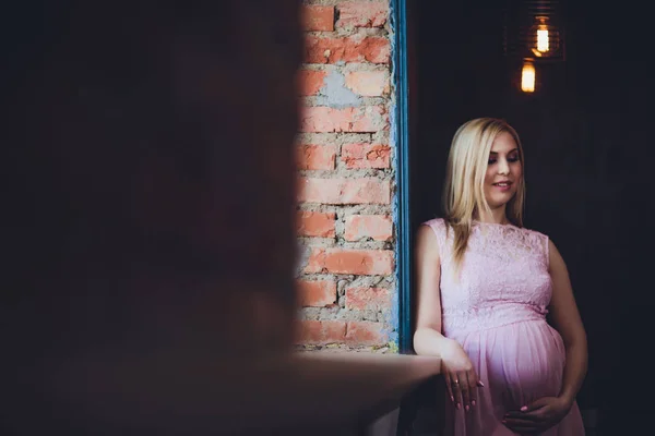 Casualmente vestito attraente donna incinta in piedi a casa, guardando la fotocamera e sorridendo mentre — Foto Stock