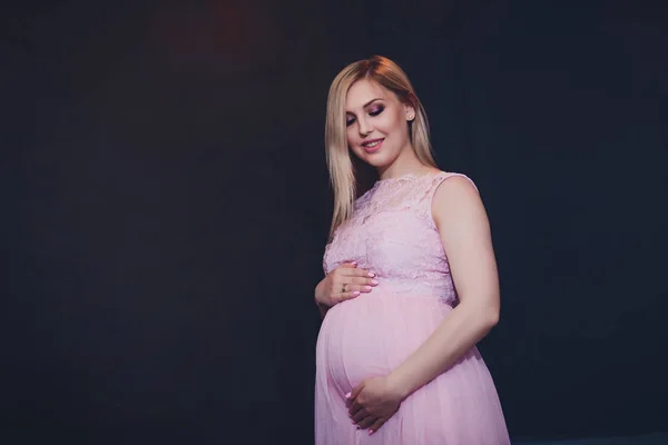 Casualmente vestido mulher grávida atraente em pé em casa, olhando câmera e sorrindo enquanto — Fotografia de Stock