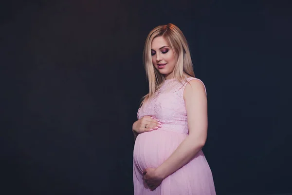Casualmente vestito attraente donna incinta in piedi a casa, guardando la fotocamera e sorridendo mentre — Foto Stock