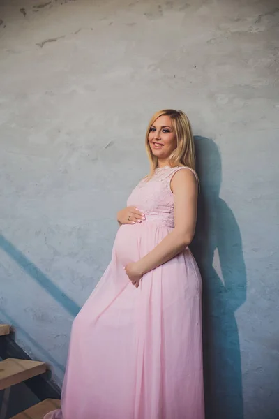 Lazán öltözött vonzó terhes nő állandó otthon, kamera keres, és mosolyogva, miközben — Stock Fotó