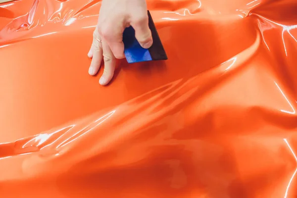 Car wrapping specialist putting vinyl foil or film car wrapping protective film yacht, boat, ship, car, mobile home. orange film heating with hair dryer and trimming plastic soft hard squeegee