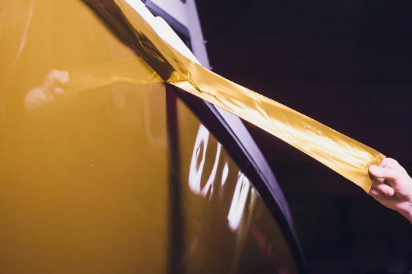 Auto wrapping specialist aanbrengen van vinyl folie of film op auto inwikkeling beschermfolie jacht, boot, schip, auto, mobile home. geel gouden film hand trekt — Stockfoto