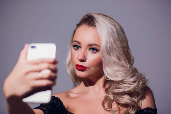 Sprawia, że piękno portret pięknej blondynce na białym tle z idealny makijaż selfie na smartfonie. — Zdjęcie stockowe