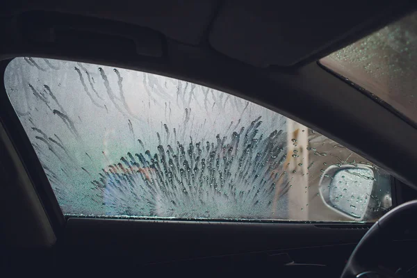 Attraktiv kvinna Tvätta bil manuell bil tvätt självbetjäning, rengöring med skum, pressade vatten. Tvätta bilen i self service station med högtryck blaster fönster tittade på från bilen — Stockfoto