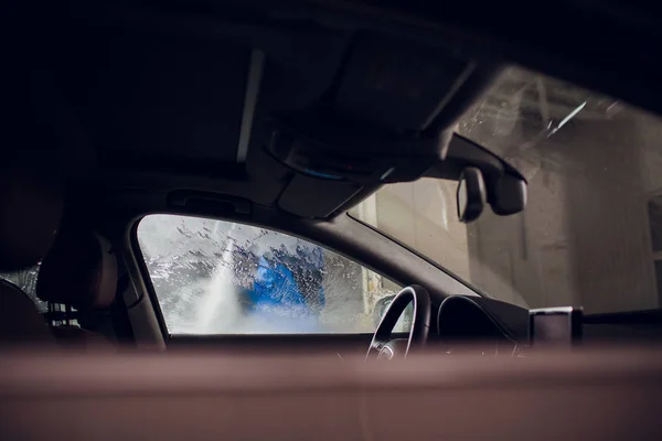 man washing automobile manual car washing self service,cleaning with foam,pressured water. Washing car in self service station with high pressure blaster window viewed from inside car